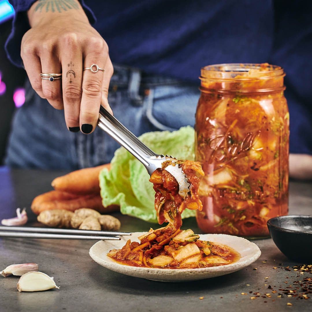 Kimchi läggs upp på en tallrik, i bakgrunden en burk med kimchi