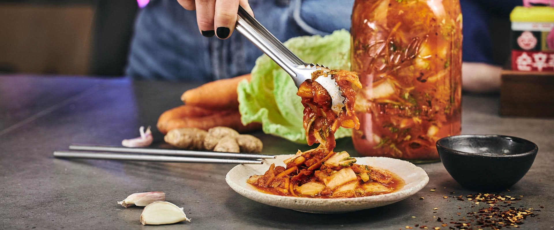 Kimchi läggs upp på en tallrik, i bakgrunden en burk med kimchi