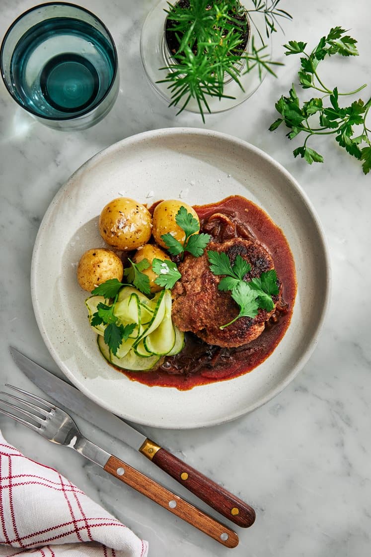 Pannbiff med löksky, pressgurka, rårörda lingon och kokt potatis